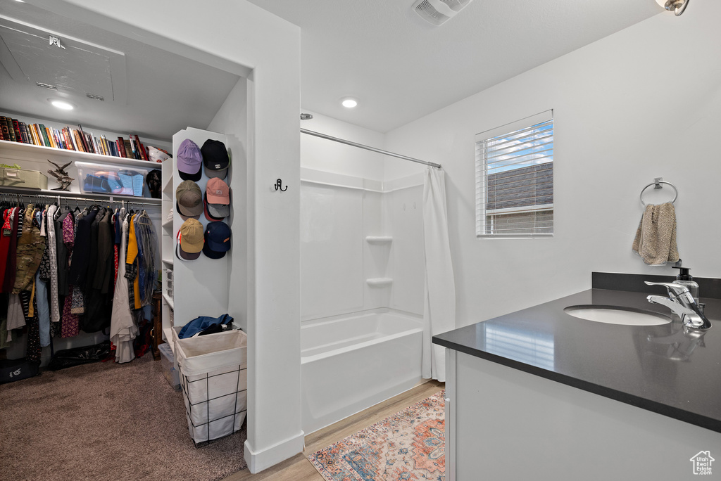 Bathroom with a spacious closet, wood finished floors, shower / bath combination with curtain, vanity, and recessed lighting