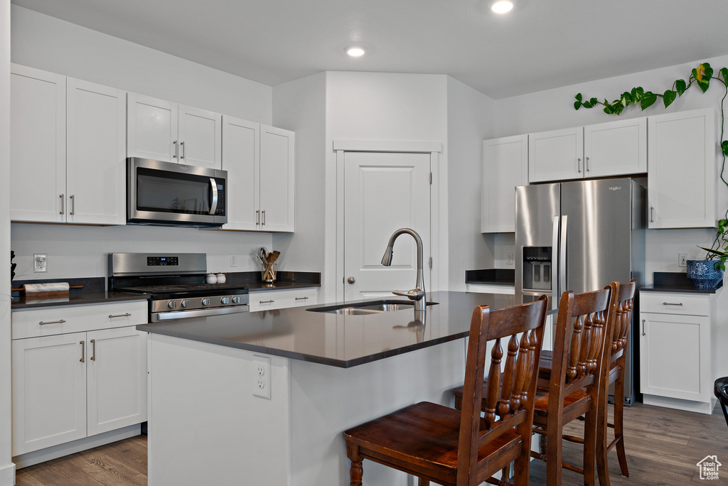 Kitchen with stainless steel appliances, a sink, dark countertops, a kitchen bar, and dark wood-type flooring