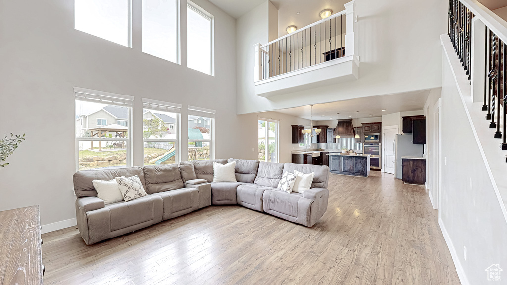 Living area featuring stairs, light wood-style floors, a towering ceiling, and baseboards