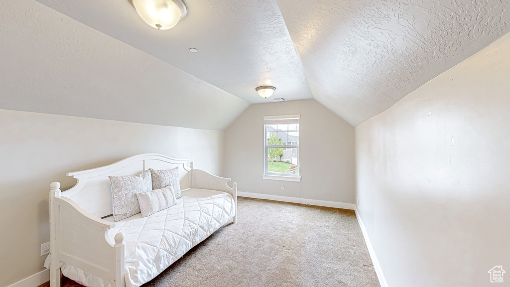 Carpeted bedroom with a textured ceiling, baseboards, and lofted ceiling