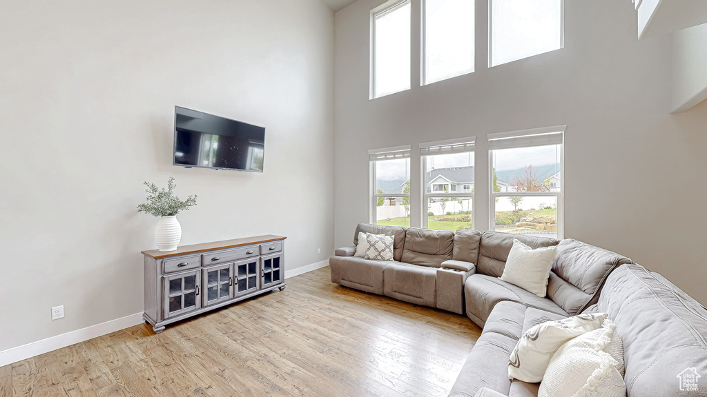 Living area with baseboards, light wood-style floors, and a towering ceiling