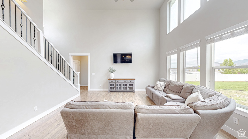 Living room with a towering ceiling, stairway, light wood-style flooring, baseboards, and ceiling fan