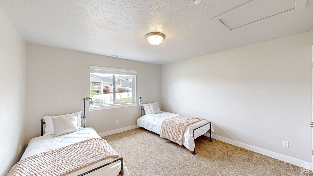 Carpeted bedroom with attic access, baseboards, and a textured ceiling