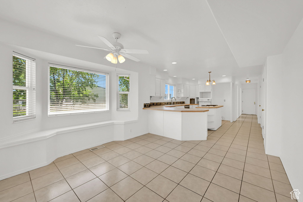 Kitchen featuring a peninsula, light tile patterned floors, white cabinetry, healthy amount of natural light, and recessed lighting