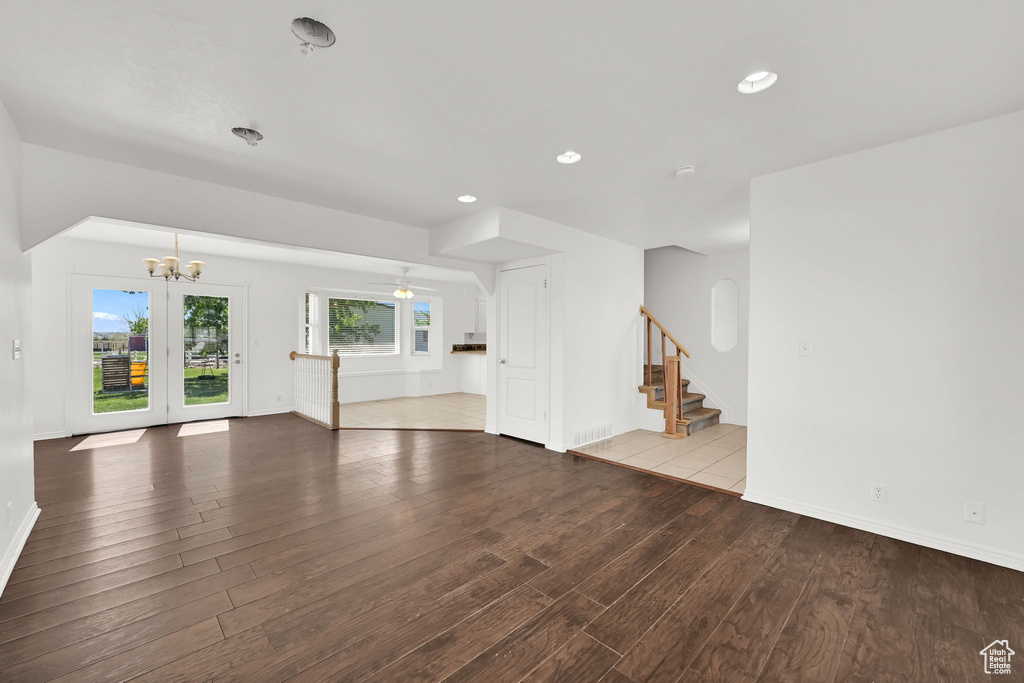 Unfurnished living room with wood finished floors, stairs, a chandelier, baseboards, and recessed lighting
