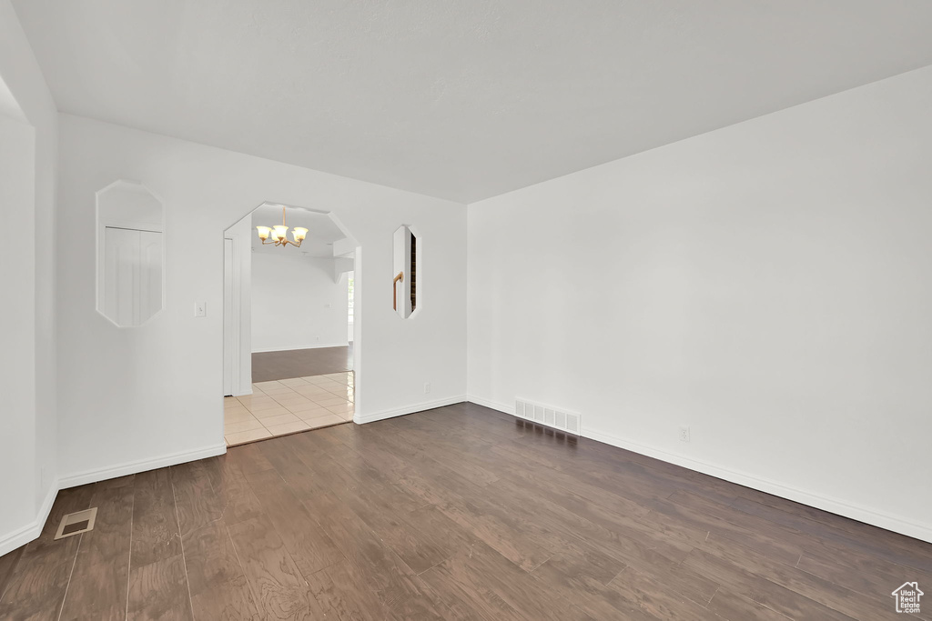 Unfurnished room with arched walkways, dark wood-type flooring, a chandelier, and baseboards