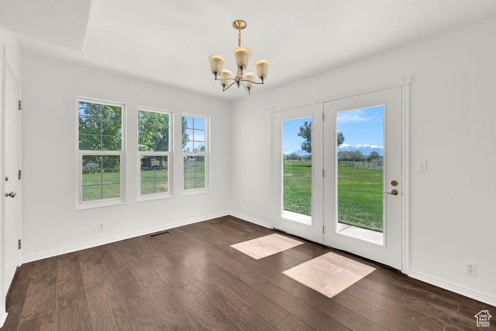 Unfurnished dining area with a chandelier, dark wood-type flooring, and baseboards