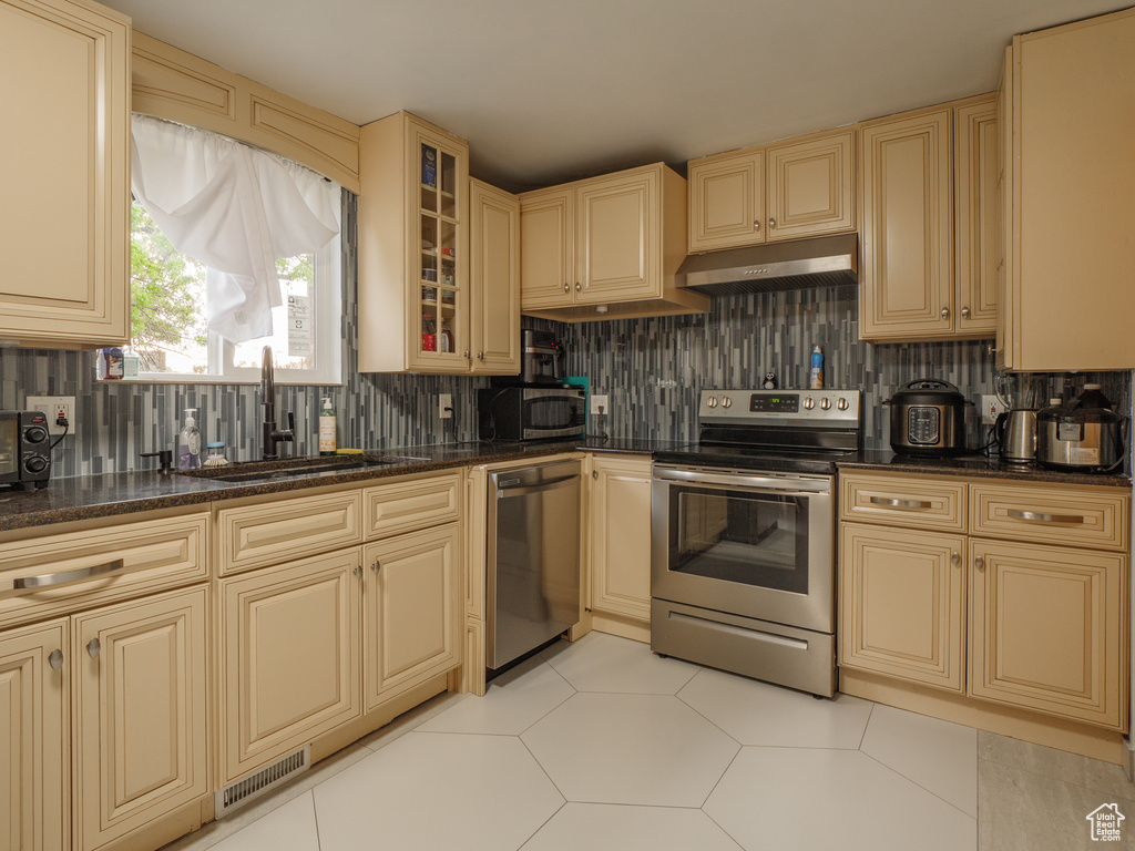 Kitchen featuring appliances with stainless steel finishes, cream cabinets, under cabinet range hood, and a sink