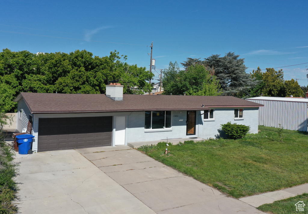 Ranch-style home with an attached garage, a front lawn, driveway, a chimney, and roof with shingles