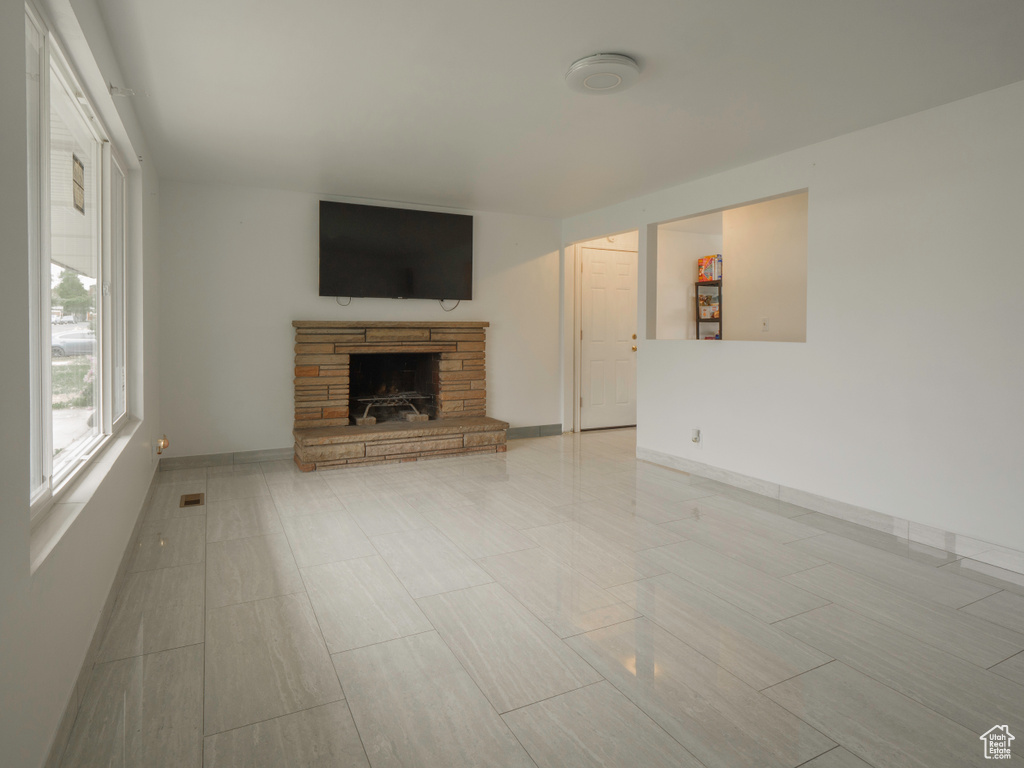 Unfurnished living room featuring a fireplace with raised hearth and baseboards