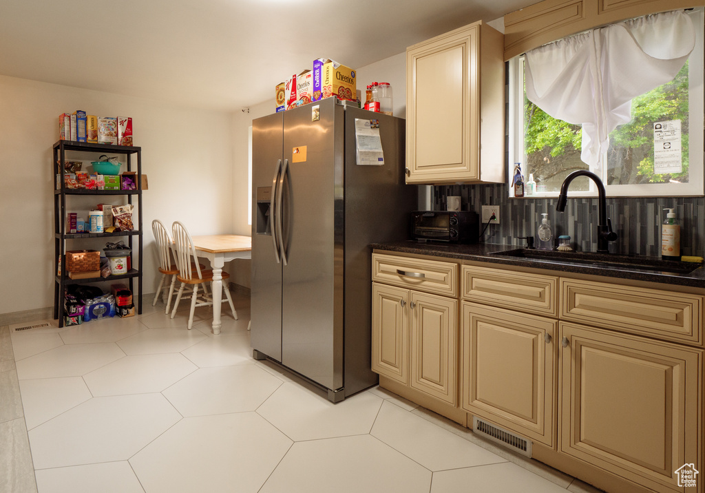 Kitchen featuring stainless steel refrigerator with ice dispenser, a sink, dark countertops, cream cabinets, and tasteful backsplash