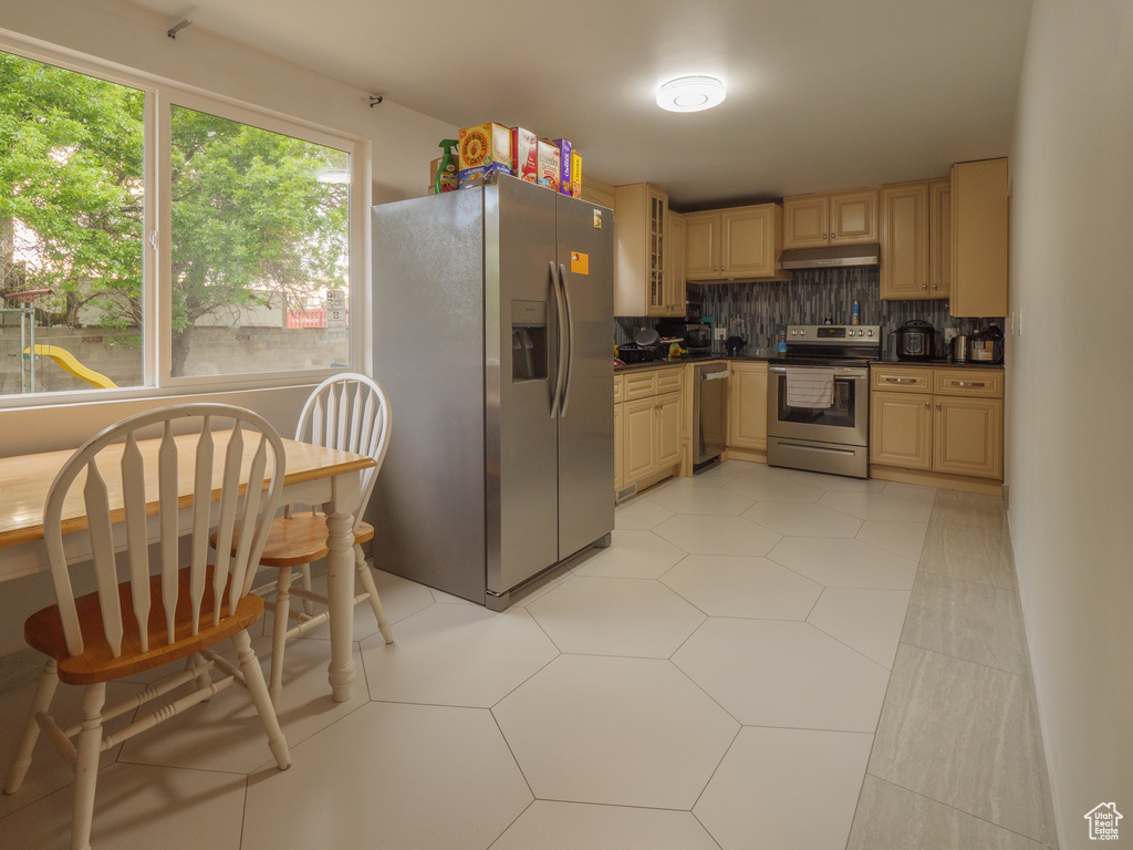 Kitchen featuring appliances with stainless steel finishes, under cabinet range hood, dark countertops, backsplash, and glass insert cabinets