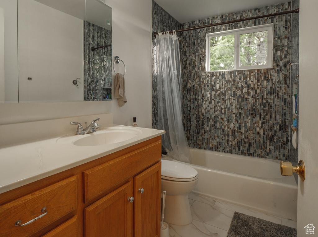 Bathroom featuring shower / bathtub combination with curtain, toilet, vanity, and marble finish flooring