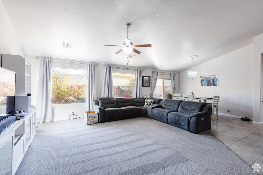 Living area with light tile patterned floors, visible vents, baseboards, vaulted ceiling, and ceiling fan with notable chandelier