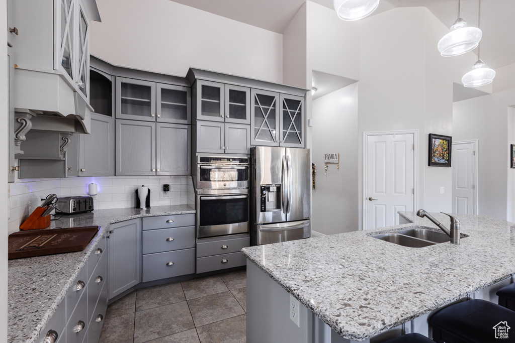 Kitchen featuring gray cabinets, stainless steel appliances, backsplash, a sink, and a kitchen breakfast bar