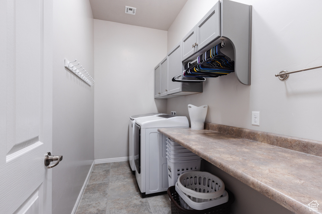 Clothes washing area featuring baseboards, visible vents, washer and dryer, and cabinet space