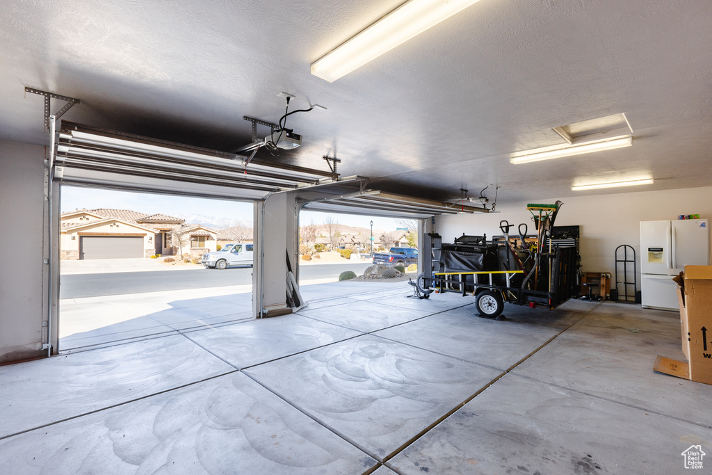 Garage featuring a garage door opener and white refrigerator with ice dispenser