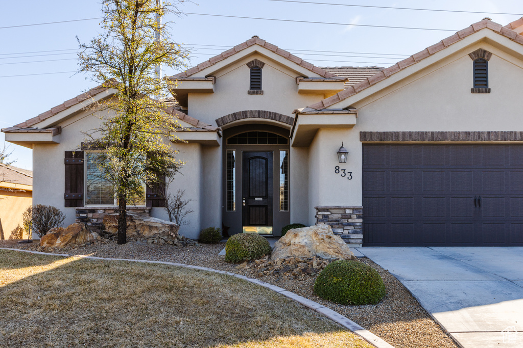 Mediterranean / spanish-style home featuring a garage, stone siding, a tiled roof, concrete driveway, and stucco siding
