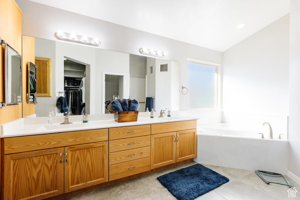 Full bath featuring double vanity, a garden tub, lofted ceiling, and a sink