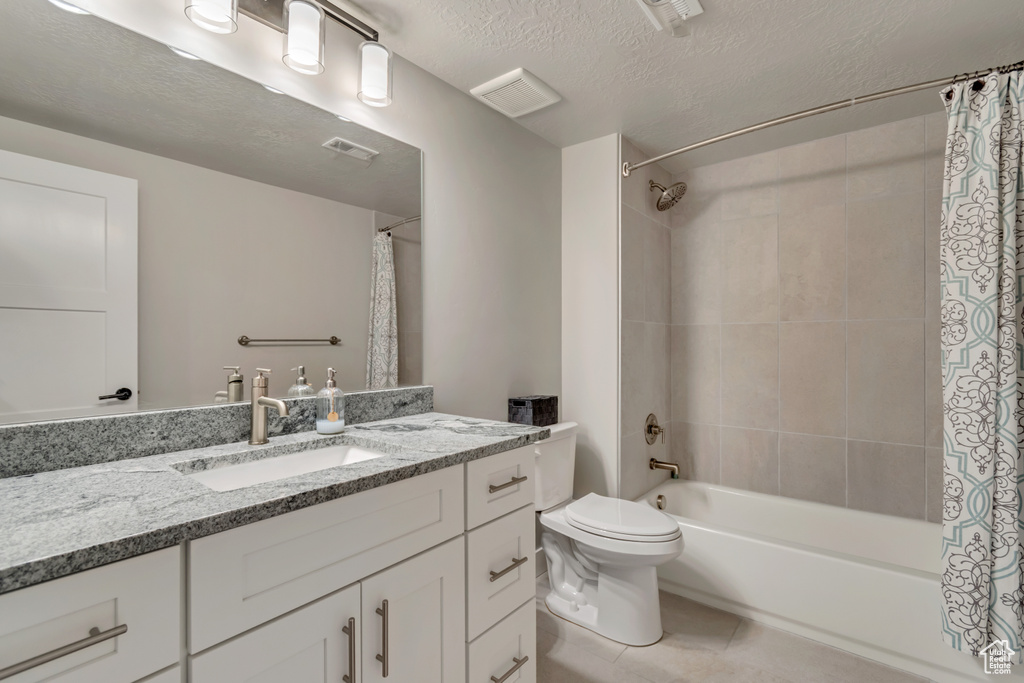 Bathroom with shower / bath combination with curtain, toilet, vanity, tile patterned floors, and a textured ceiling