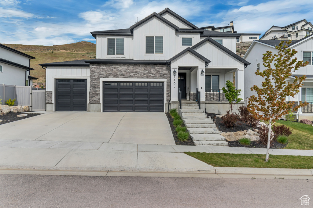 View of front of home with board and batten siding, concrete driveway, a gate, stone siding, and fence