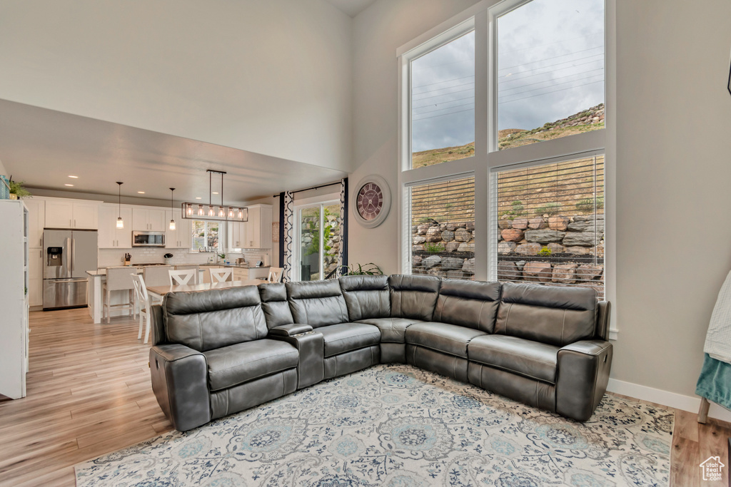Living room with light wood-type flooring, baseboards, recessed lighting, and a high ceiling