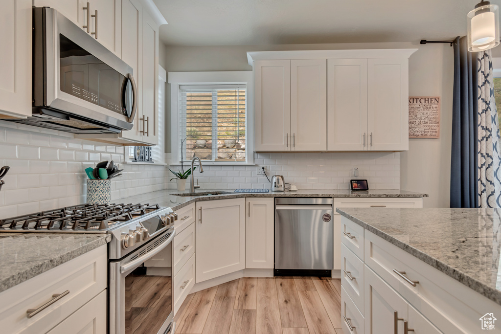 Kitchen featuring stainless steel appliances, a sink, light wood-type flooring, and white cabinetry