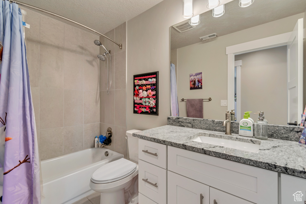 Bathroom featuring shower / tub combo, toilet, vanity, and a textured ceiling