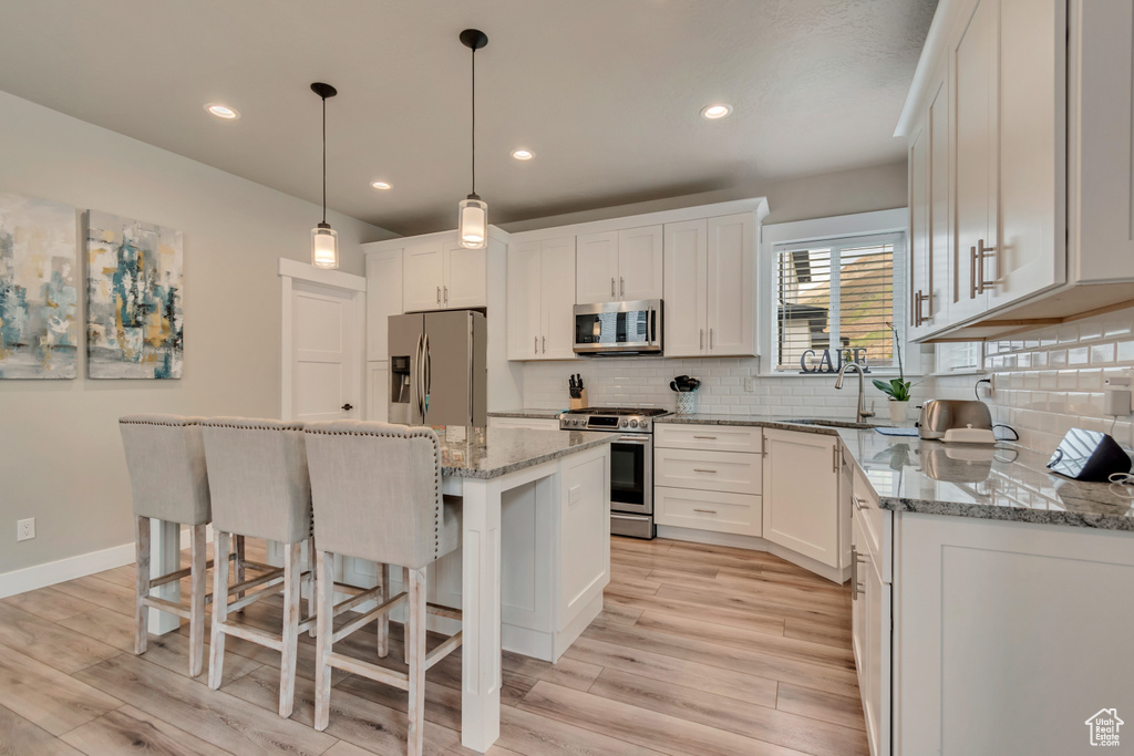 Kitchen with stainless steel appliances, light wood-type flooring, a breakfast bar, white cabinets, and recessed lighting