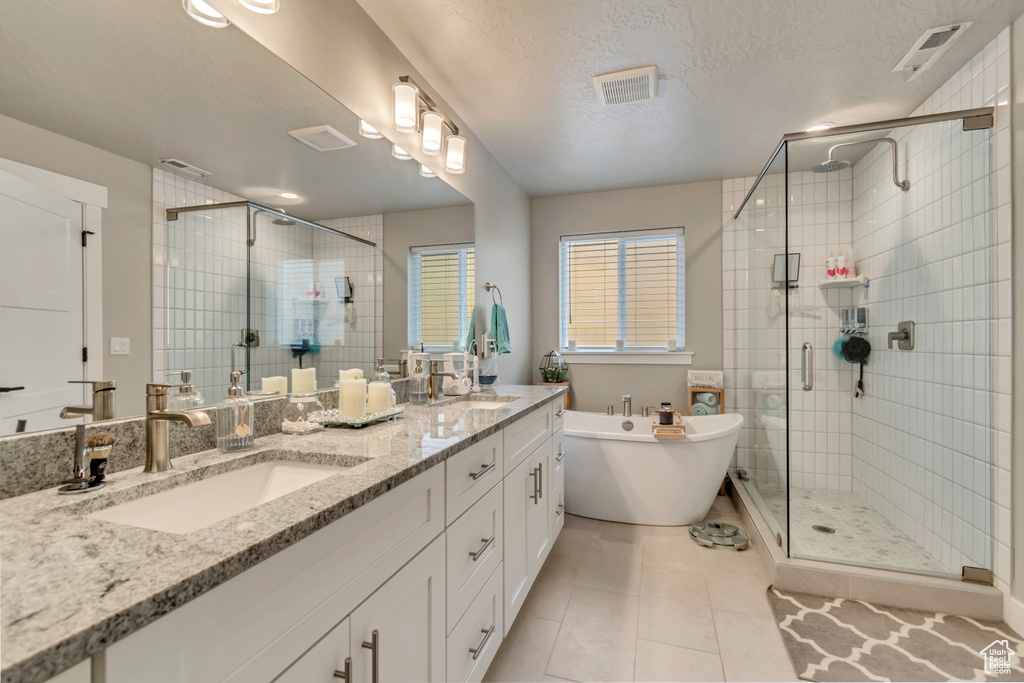 Bathroom with a stall shower, a soaking tub, double vanity, tile patterned floors, and a textured ceiling