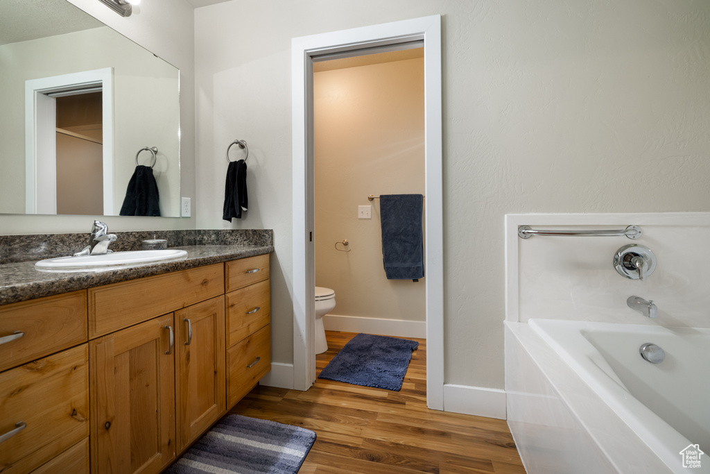 Full bath featuring wood finished floors, vanity, toilet, a tub to relax in, and baseboards