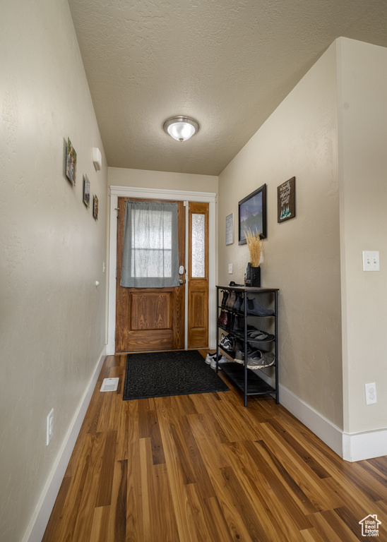 Doorway with wood finished floors, baseboards, and a textured ceiling