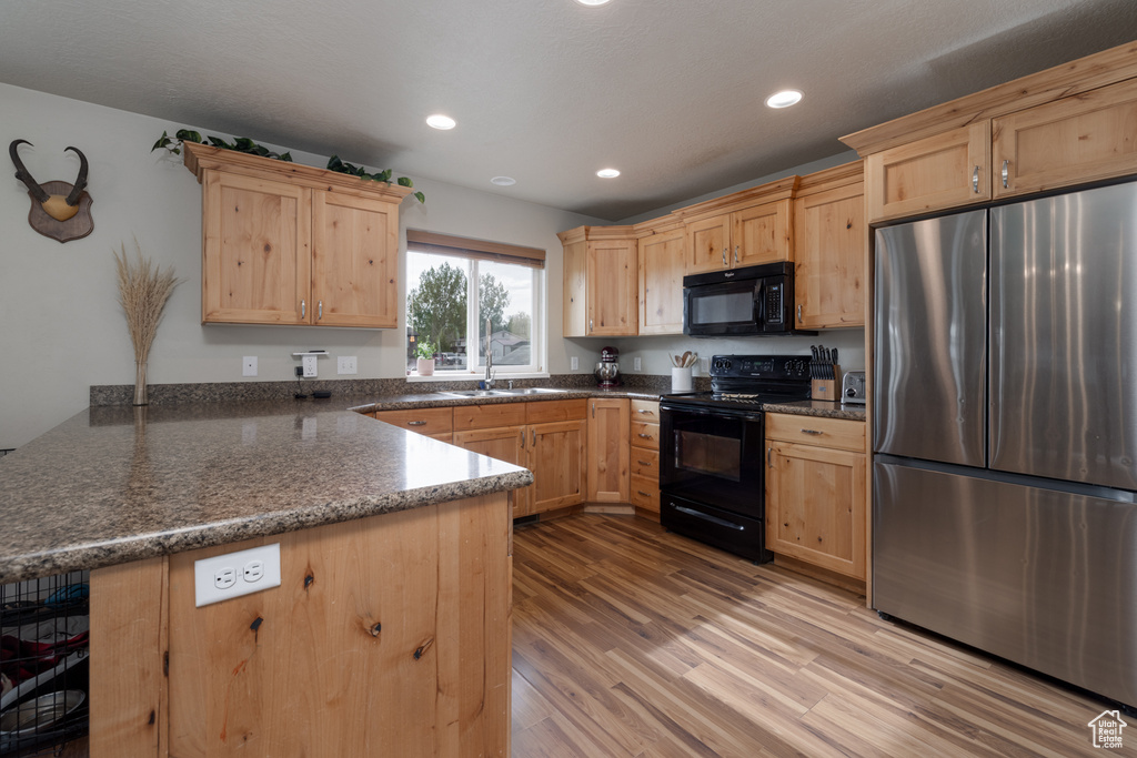 Kitchen with black appliances, a peninsula, light brown cabinetry, a sink, and recessed lighting