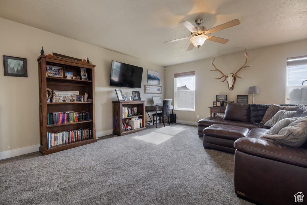 Carpeted living room featuring a ceiling fan and baseboards