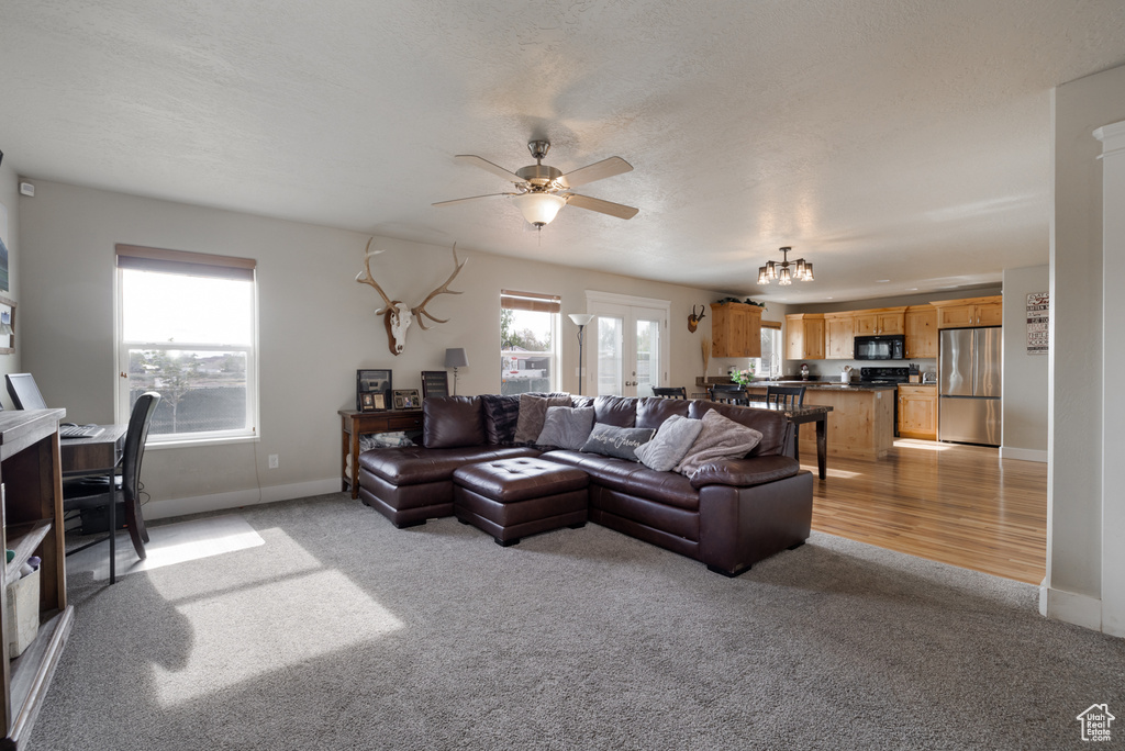 Living area with light carpet, a ceiling fan, baseboards, and a chandelier