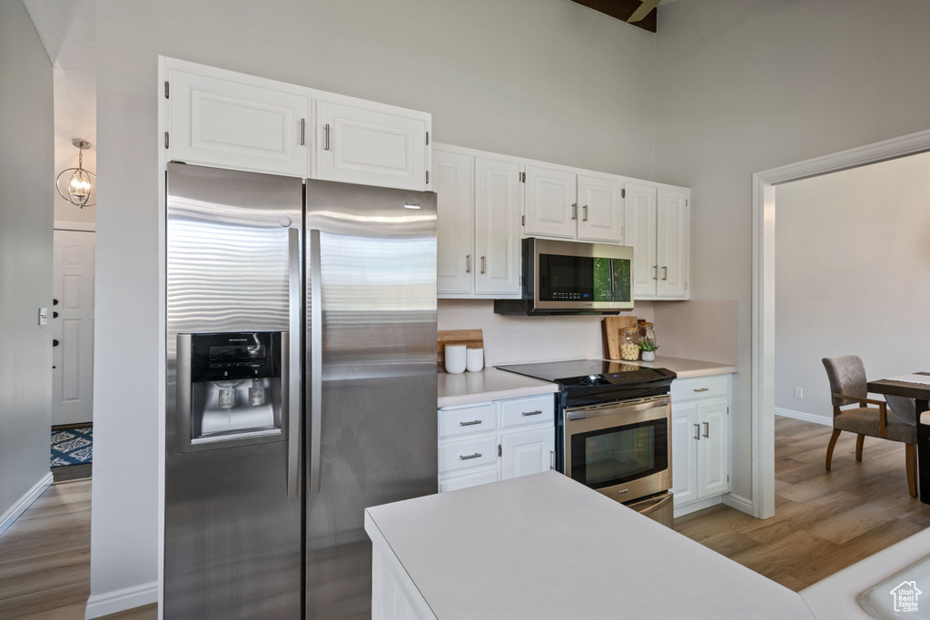 Kitchen with appliances with stainless steel finishes, light wood-type flooring, white cabinetry, light countertops, and a towering ceiling