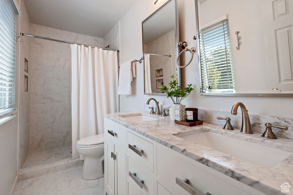 Bathroom featuring marble finish flooring, toilet, a tile shower, and double vanity