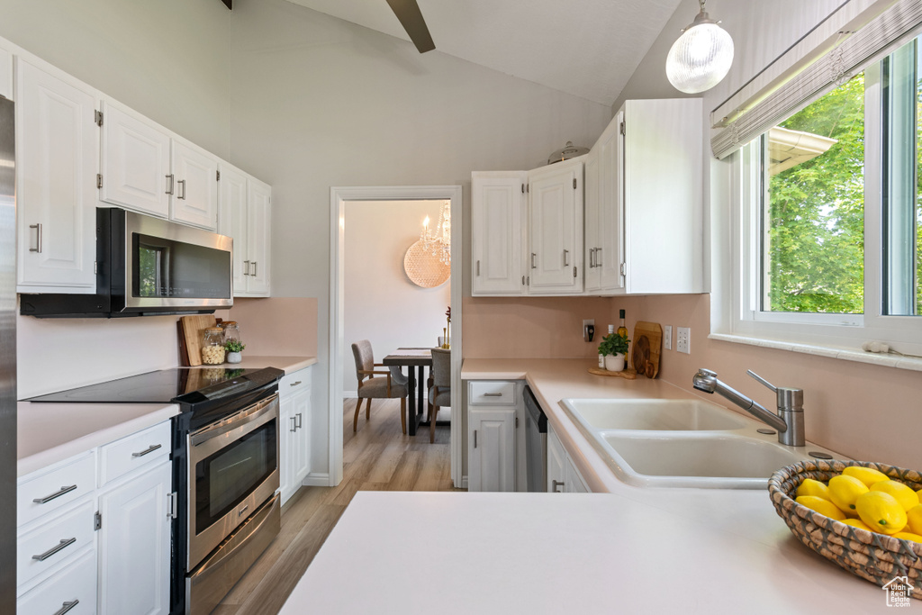 Kitchen with stainless steel appliances, a sink, light countertops, white cabinetry, and light wood finished floors