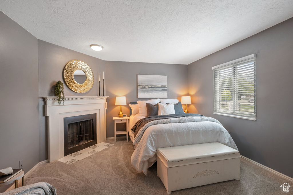 Bedroom with carpet, baseboards, a fireplace with flush hearth, and a textured ceiling