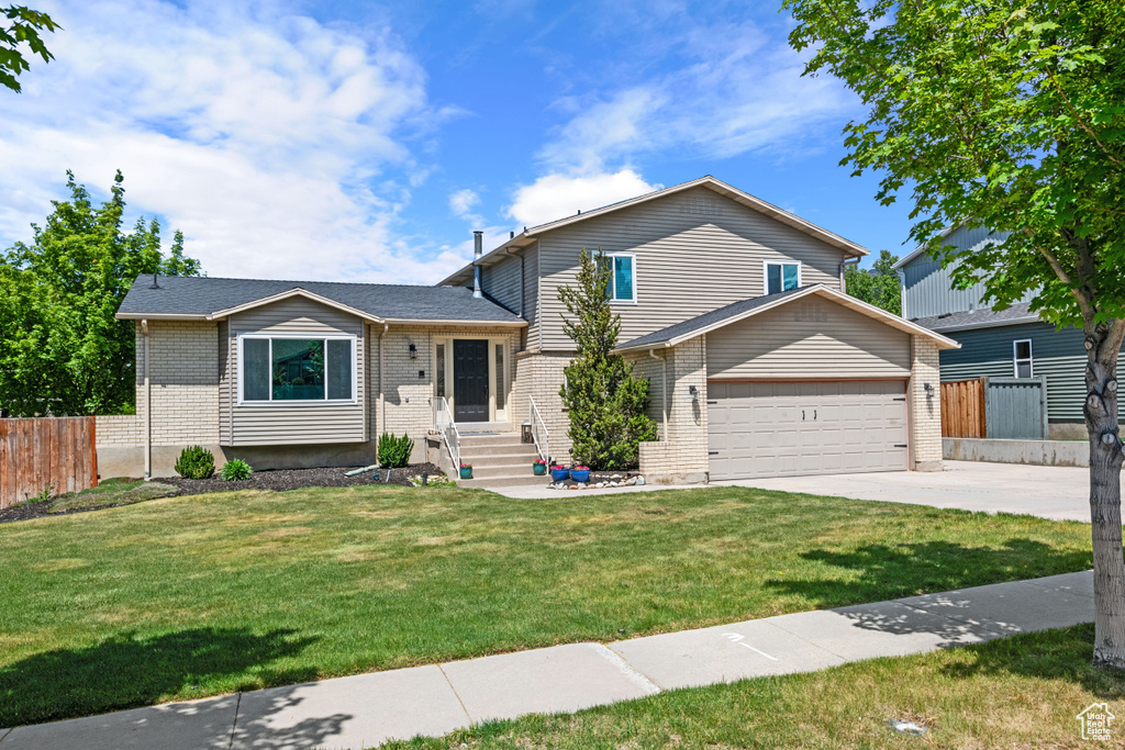 Tri-level home featuring driveway, brick siding, and a garage