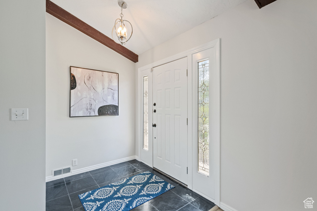 Entryway featuring lofted ceiling, baseboards, a chandelier, and dark tile patterned flooring