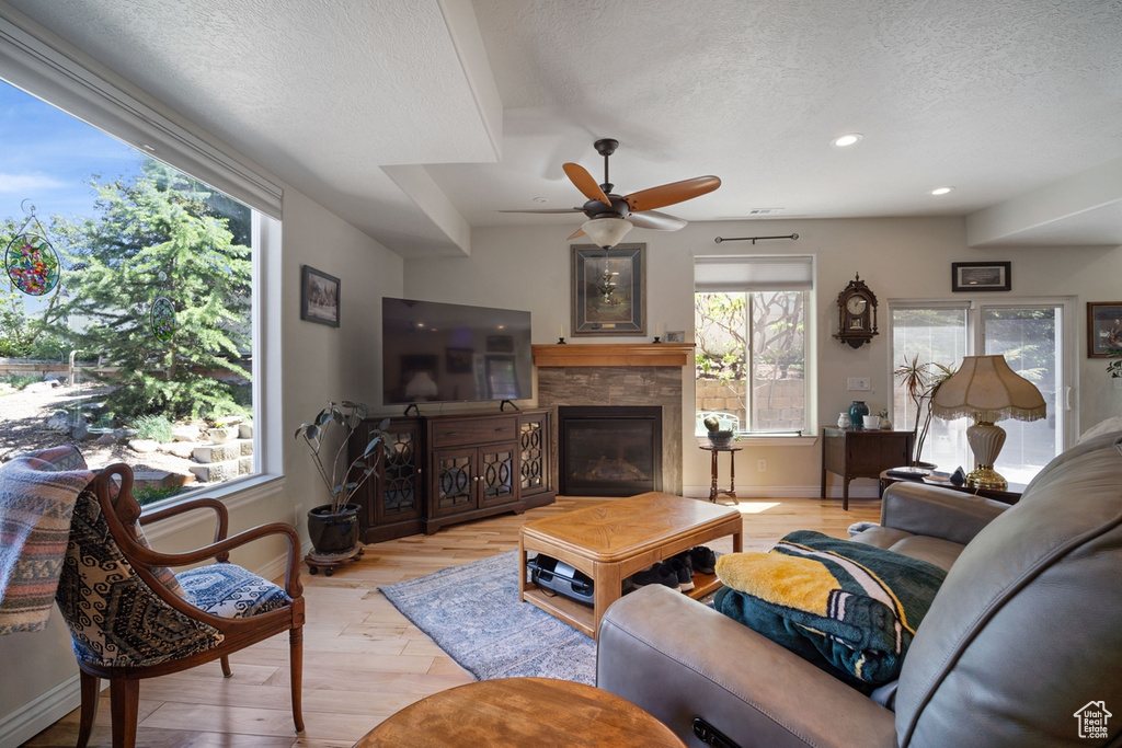 Living room featuring a textured ceiling, light wood-style flooring, a stone fireplace, baseboards, and recessed lighting