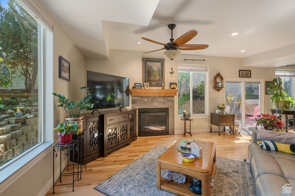 Living area with a glass covered fireplace, a ceiling fan, wood finished floors, recessed lighting, and baseboards