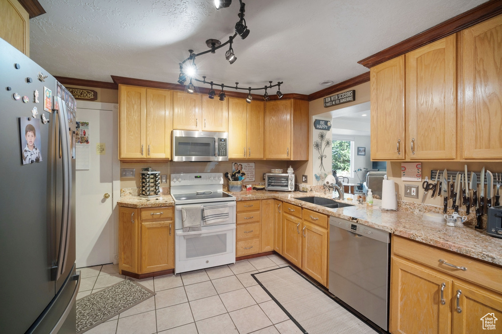 Kitchen featuring stainless steel appliances, a sink, light tile patterned floors, light stone counters, and crown molding