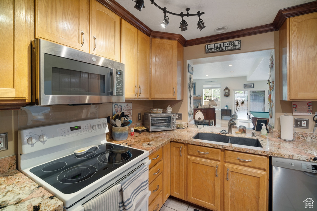 Kitchen featuring stainless steel appliances, a sink, crown molding, light stone counters, and light tile patterned floors