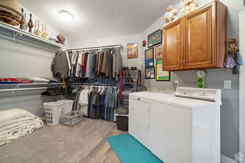 Laundry area with washer and clothes dryer, cabinet space, light wood-type flooring, and a textured ceiling