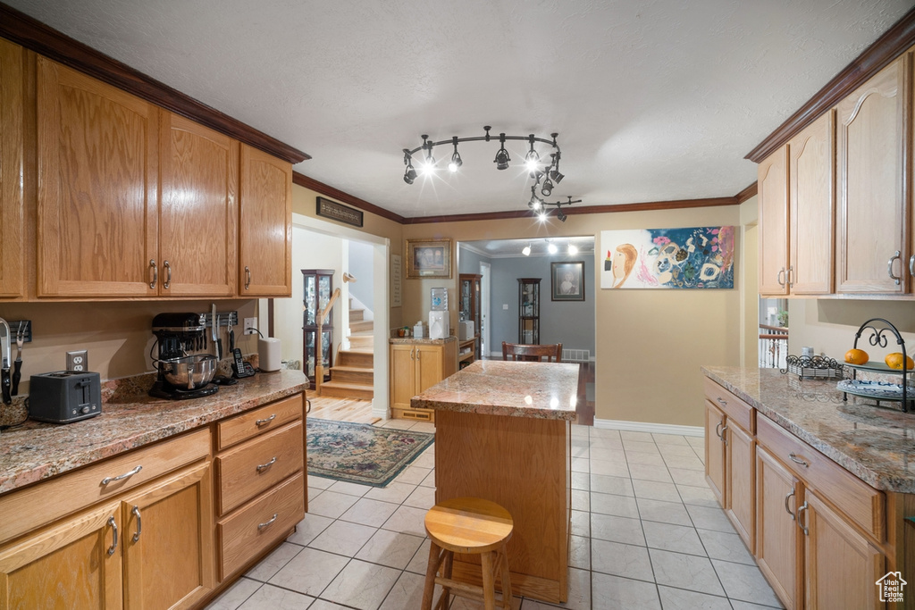 Kitchen featuring light tile patterned flooring, a center island, light stone counters, crown molding, and baseboards