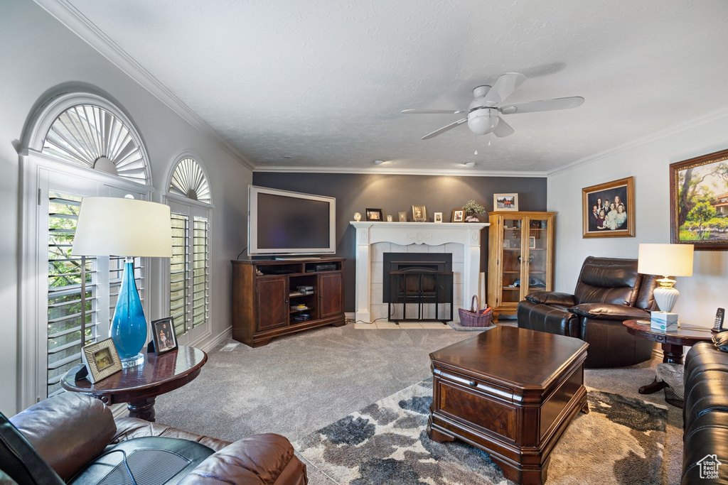 Carpeted living area with a ceiling fan, crown molding, a fireplace with flush hearth, and baseboards
