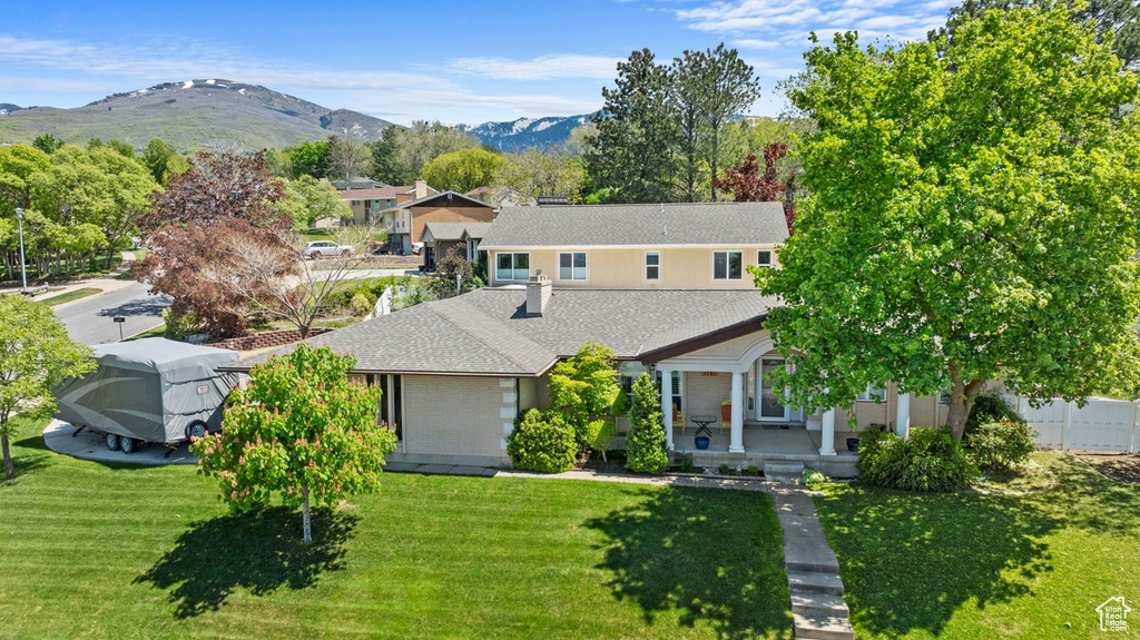 View of front of house featuring a front yard, covered porch, a mountain view, and a shingled roof