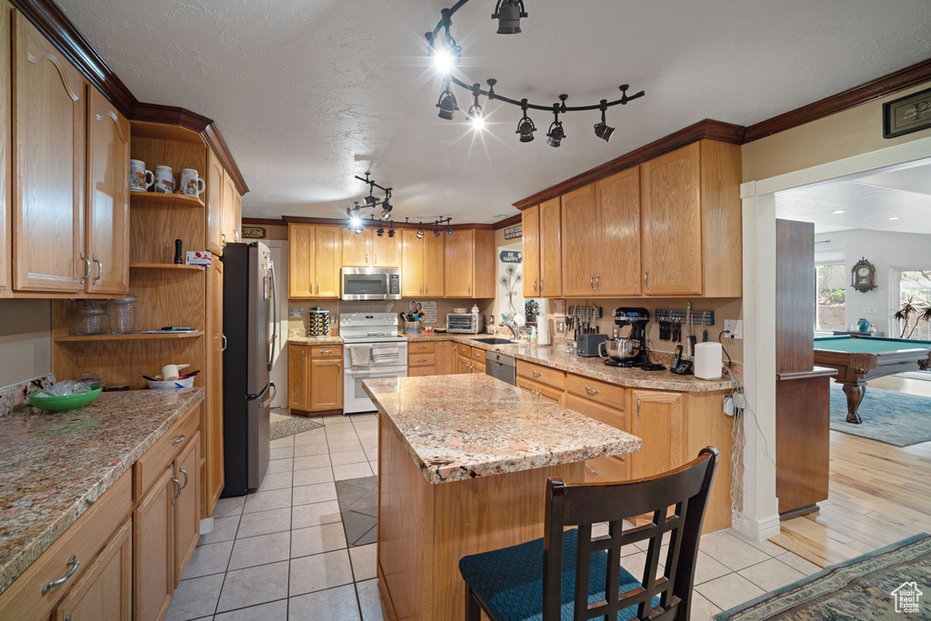 Kitchen with appliances with stainless steel finishes, open shelves, light tile patterned floors, a kitchen island, and crown molding